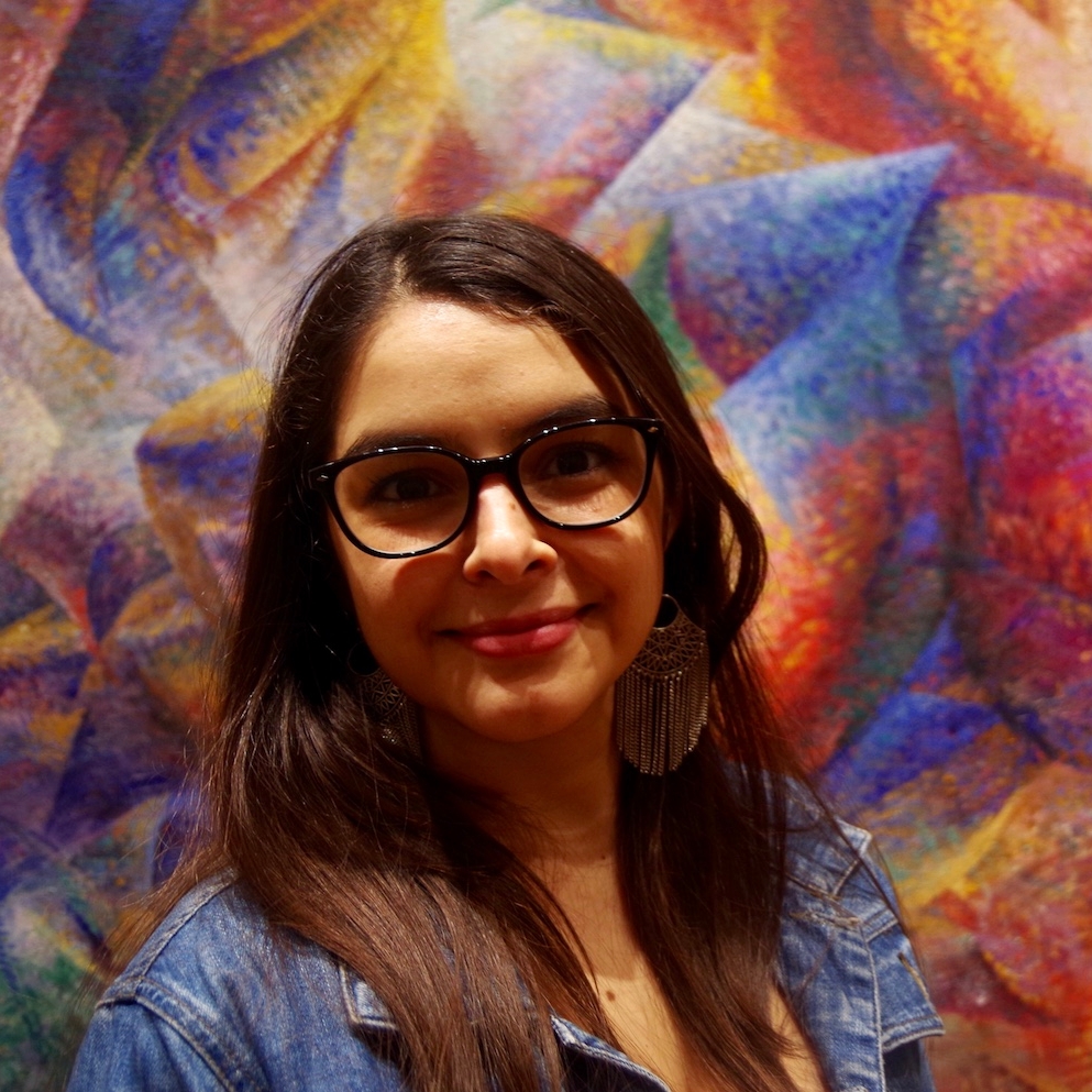 long brown hair with glasses, in front of blue and red wall wearing denim shirt